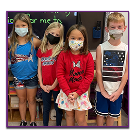 Four students posing in the classroom with masks